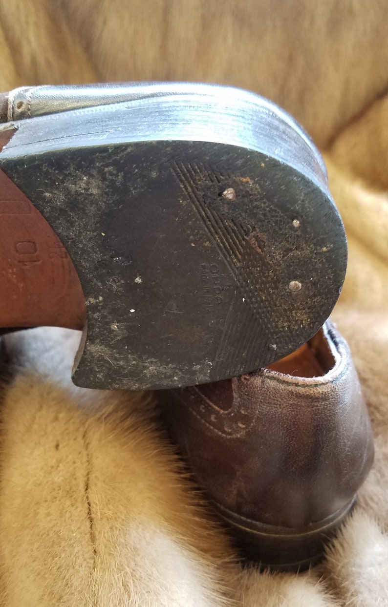 May include: Close-up of the bottom of a brown leather shoe with a black rubber sole. The sole has a textured pattern and the words "Oxford Made in India" are visible.