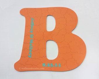 Könnte beinhalten: Orangefarbenes Holzpuzzle in Form des Buchstabens B. Das Puzzle ist mit den Namen "Jeffrey & Mallory" und dem Datum "8.23.14" verziert.