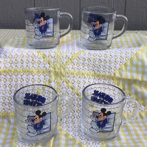 May include: Four clear glass mugs featuring Mickey Mouse in a blue suit, with the words "BREAK TIME" in blue. The mugs have a handle and are decorated with horizontal blue lines.