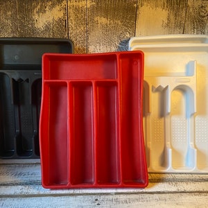 May include: Three plastic utensil organizers in black, red, and white. The black and white organizers have slots for knives, forks, and spoons. The red organizer has four long compartments. These organizers are designed for kitchen storage.