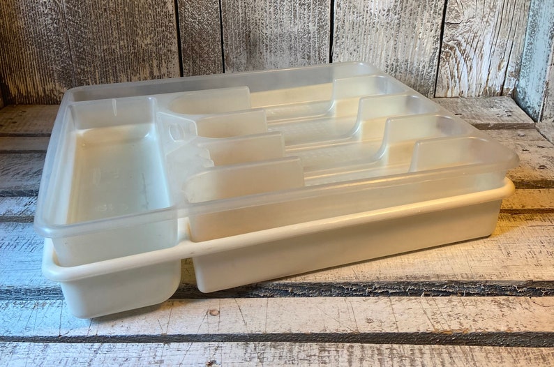 Pode incluir: Uma bandeja de talheres de pl&aacute;stico transparente com v&aacute;rios compartimentos para organizar a prataria. A bandeja &eacute; de cor branco sujo e tem formato retangular com v&aacute;rias ranhuras e divis&oacute;rias. &Eacute; projetada para caber dentro de uma gaveta de cozinha.