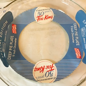 May include: Clear glass deep pie plate, 9-inch diameter, with a blue and white label that reads "Special Edition" and "Fire-King Commemorating 50 years." The plate is microwave safe.