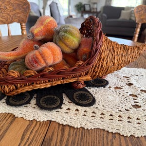 May include: A woven cornucopia basket filled with a collection of small, textured, sugar-coated decorative gourds and pumpkins in shades of orange, yellow, and green. The basket is crafted from brown natural fibers with a braided rim detail.