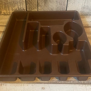 Pode incluir: Uma bandeja de talheres de pl&aacute;stico castanho com v&aacute;rios compartimentos para organizar a prataria. A bandeja tem sec&ccedil;&otilde;es para garfos, facas, colheres e outros utens&iacute;lios. Concebida para caber dentro de uma gaveta de cozinha.