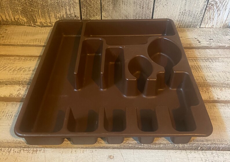 Pode incluir: Uma bandeja de talheres de pl&aacute;stico castanho com v&aacute;rios compartimentos para organizar a prataria. A bandeja tem sec&ccedil;&otilde;es para garfos, facas, colheres e outros utens&iacute;lios. Concebida para caber dentro de uma gaveta de cozinha.