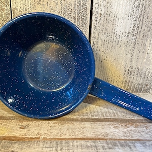 May include: A blue enamelware saucepan with a long handle and white speckles. The pan is set against a weathered wood background, showcasing a classic camping or kitchenware item.