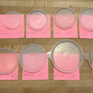 May include: A collection of clear plastic lids of varying sizes, each resting on a pink sticky note with handwritten numbers and inch measurements. The lids range from 1 1/4 inches to 4 inches in diameter.
