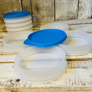 May include: A collection of round, translucent white plastic containers with bright blue lids. One container is placed in the foreground with its blue lid on, while several other containers are arranged around it, some stacked and some open.