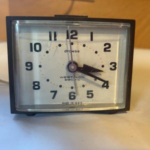 May include: A vintage black Westclox electric alarm clock with a white face. The clock has black numerals and hands, with the word "drowse" above the center. The clock reads 3:59. The words "WESTCLOX electric" and "MADE IN USA" are visible.
