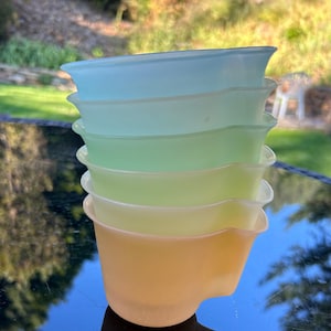 May include: A stack of six vintage Pyrex mixing bowls in pastel colors: light blue, green, and yellow. The bowls have a distinctive flared rim and a pouring spout. The bowls are stacked on a reflective surface.