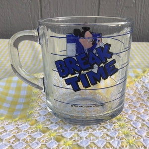 May include: Clear glass mug with a handle featuring a graphic of Mickey Mouse and the words "BREAK TIME" in blue. The mug has blue horizontal lines and the text "THE WALT DISNEY COMPANY" at the bottom.
