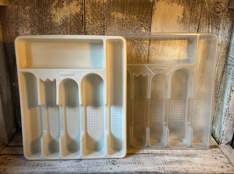 Pode incluir: Duas bandejas de talheres de pl&aacute;stico. Uma &eacute; branca opaca, a outra transl&uacute;cida. Ambas t&ecirc;m compartimentos para garfos, facas e colheres. A bandeja branca tem formato retangular, enquanto a transl&uacute;cida tem um design semelhante.