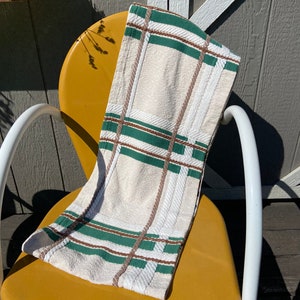 May include: A rectangular kitchen towel featuring a cream-colored base with a woven plaid pattern. The design consists of intersecting horizontal and vertical stripes in forest green and thin brown lines, creating a classic grid-like appearance.