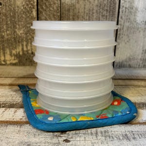 May include: A stack of six translucent, circular plastic lids with a flat top and a raised rim, resting on a blue quilted fabric pad featuring a colorful floral pattern of red, yellow, and blue flowers on a light green background.
