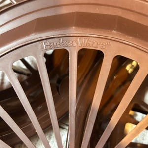 May include: Close-up of several brown PackerWare plastic lids. The lids have a radial spoke design with rectangular cutouts. The PackerWare logo is visible on the top of the lid.