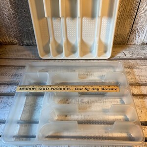 Pode incluir: Duas bandejas de talheres de pl&aacute;stico. A bandeja superior &eacute; branca suja e tem compartimentos para utens&iacute;lios. A bandeja inferior &eacute; transparente e tem compartimentos. Uma r&eacute;gua de madeira com texto est&aacute; na bandeja inferior.