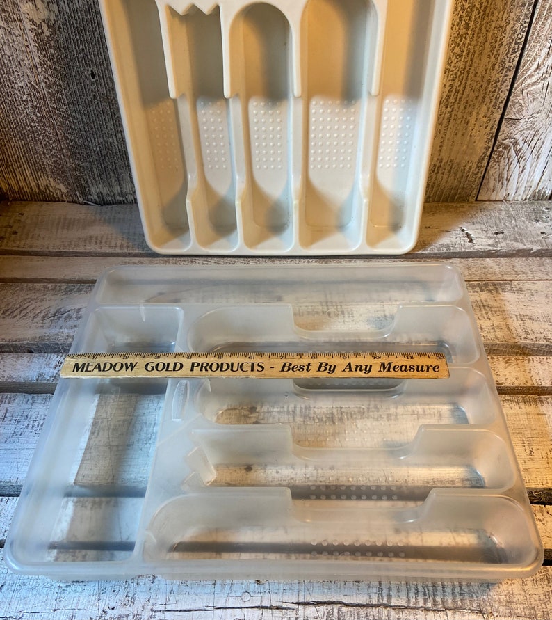 Pode incluir: Duas bandejas de talheres de pl&aacute;stico. A bandeja superior &eacute; branca suja e tem compartimentos para utens&iacute;lios. A bandeja inferior &eacute; transparente e tem compartimentos. Uma r&eacute;gua de madeira com texto est&aacute; na bandeja inferior.