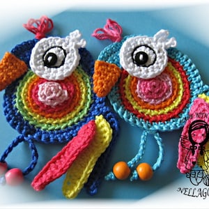 Op de afbeelding: Twee kleurrijke gehaakte vogelversieringen met regenboogkleurige cirkels en witte ogen. De vogels hebben roze, gele en oranje gehaakte staarten. De versieringen hangen aan blauwe en turquoise koorden met houten kralen.