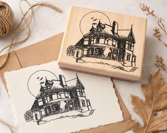May include: A rectangular wooden rubber stamp featuring a black ink illustration of a Victorian-style house with a large full moon and flying bats in the background. A ghost figure is visible on the front porch of the house design.