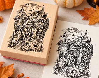 May include: A rectangular wooden rubber stamp and a matching paper print featuring a detailed black ink illustration of a haunted Victorian house with a skeleton, a witch, a ghost, a black cat, bats, and jack-o'-lanterns in the yard.