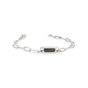May include: A silver chain bracelet with a rectangular tag. The tag has a dark gray center.