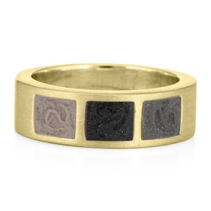 May include: A gold band ring with three square inlays. The inlays are made of a light gray, black, and dark gray material.
