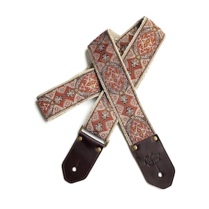 May include: A guitar strap with a red, orange, and brown paisley pattern. The strap is made of fabric and has brown leather ends with the text "Native Sons" embossed on one end.