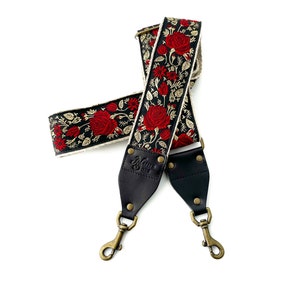 May include: A black camera strap with red and gold floral embroidery. The strap has two black leather adjustable sections with brass hardware and a "Native Sons" logo.