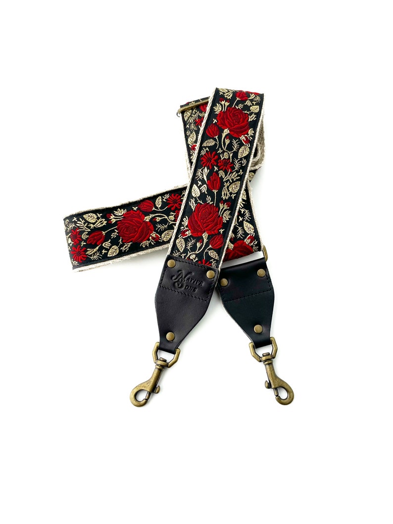 May include: A black camera strap with red and gold floral embroidery. The strap has two black leather adjustable sections with brass hardware and a "Native Sons" logo.