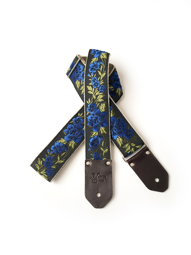 May include: A black guitar strap with a floral pattern in blue and green. The strap has brown leather ends with the text "Martin & One" embossed on one end.