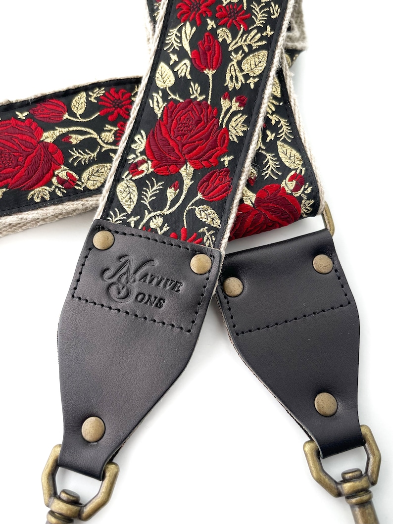 May include: Black leather camera strap with gold-tone hardware and a red and gold floral pattern. The strap is branded with "Native Sons".