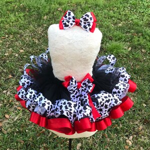 May include: A black tulle tutu with red and black and white cow print ribbon accents. A matching cow print bow is on top of the tutu.