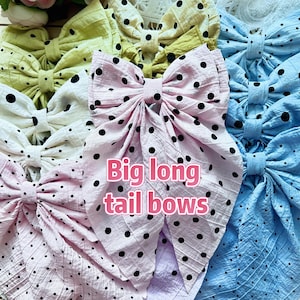May include: A collection of large fabric bows in various colors, including pink, blue, yellow, and white. Each bow features a polka dot pattern and the text "Big long tail bows". The bows are arranged closely together.