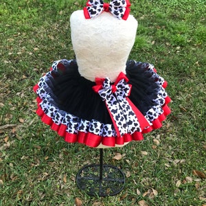 May include: Black tulle tutu skirt with red and black and white cow print ribbon trim. A matching black and white cow print bow is included.