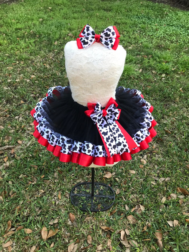 May include: Black tulle tutu skirt with red and black and white cow print ribbon trim. A matching black and white cow print bow is included.