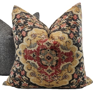 May include: A decorative throw pillow with a colorful, intricate pattern featuring a central medallion design in shades of red, gold, and blue. The background is a dark black with floral accents.