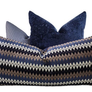 May include: Three decorative throw pillows in shades of blue, brown, and white. The largest pillow has a geometric diamond pattern. The other two pillows have textured and patterned designs. The pillows are arranged against a white background.