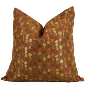 May include: A decorative throw pillow with a brown background and a pattern of vertical rows of colorful circles in shades of orange, gold, and red. The pillow is square and has a soft, textured appearance.