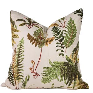 May include: A square throw pillow featuring a cream-colored fabric base decorated with a botanical print of various fern leaves in shades of forest green, olive, and rust brown. The design displays multiple fern fronds and stems across the surface.