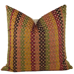 May include: A decorative throw pillow with a geometric pattern in shades of red, orange, yellow, green, and brown. The pillow is made of a textured fabric and has a square shape.
