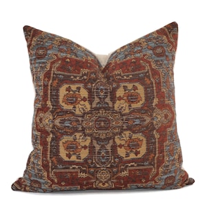 May include: A decorative throw pillow with a colorful, intricate pattern reminiscent of a traditional rug. The pillow features a central medallion design with repeating floral motifs in shades of brown, orange, blue, and red.