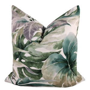 May include: A decorative throw pillow featuring a watercolor design of large tropical leaves in shades of green, gray, and white. The pillow has a soft, textured appearance, perfect for adding a touch of nature-inspired decor to any living space.