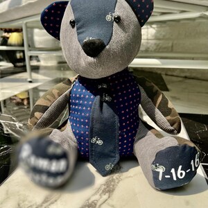 K&ouml;nnte beinhalten: Ein handgefertigter Teddyb&auml;r im Patchwork-Design. Der B&auml;r hat einen grauen K&ouml;rper, marineblaue Akzente mit Fahrradmustern und Tarnfarbenarme. Der B&auml;r hat eine marineblaue Krawatte und das Datum "7-16-16" auf einem Fu&szlig;.
