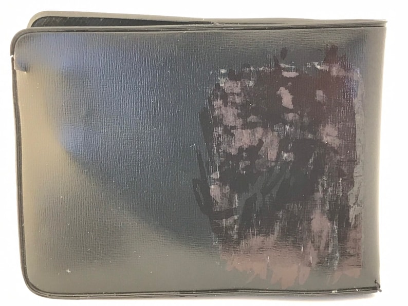 May include: A black leather wallet with a faded, abstract design on the front.