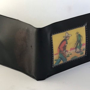 May include: Black leather wallet with a clear plastic window displaying a vintage comic book illustration of two cowboys in a desert setting.