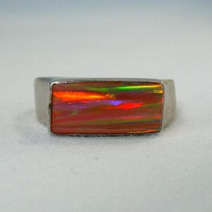 May include: A silver ring featuring a rectangular opal gemstone. The opal exhibits a spectrum of colours, including red, orange, and green. The ring has a simple, contemporary design.