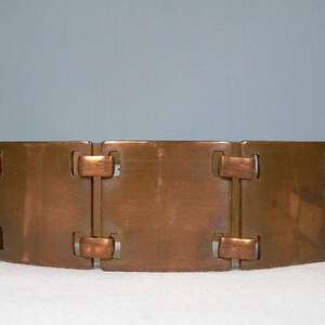 Op de afbeelding: Een koperen armband met rechthoekige schakels verbonden door kleinere staven. De armband heeft een warme, metallic tint en een geometrisch ontwerp. De schakels zijn ongeveer 2,5 cm breed.