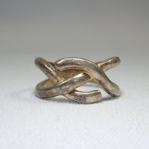 May include: A silver ring with a unique, interwoven design. The ring is made of a single piece of metal that is twisted and turned to create a complex pattern.