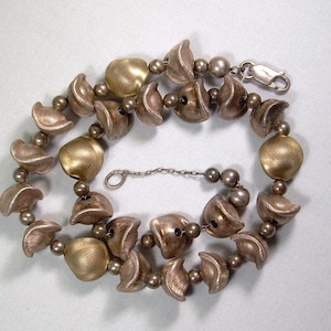 May include: A silver necklace featuring a combination of textured, shell-shaped and round beads. Some beads have a gold finish. The necklace is fastened with a silver clasp.