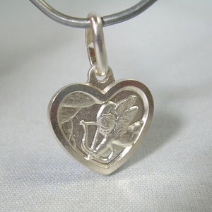 May include: A silver heart-shaped pendant with a detailed engraving of Cupid holding a bow and arrow. The pendant is suspended from a silver chain, showcasing a romantic theme. The design is intricate and the metal has a polished finish.